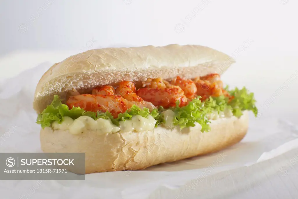 Baguette roll filled with crayfish against white background.