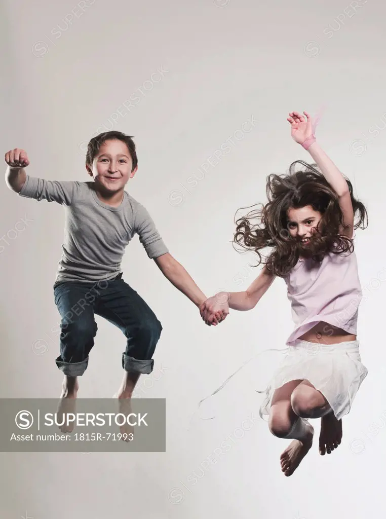 Boy and girl 8_9 holding hands and jumping, smiling, portrait