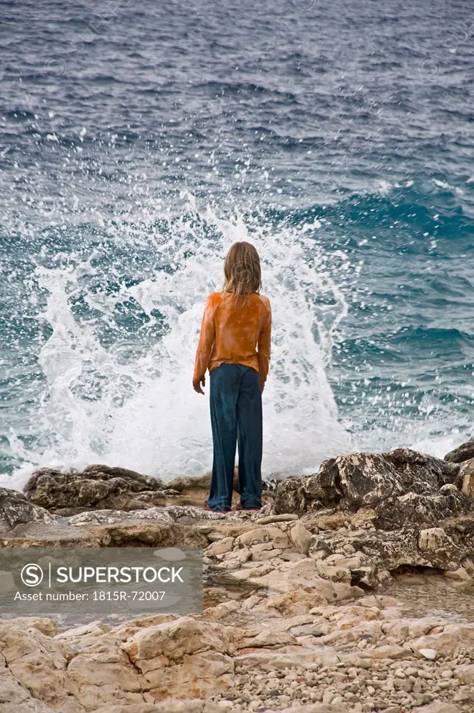 Croatia, Korcula, Girl 8_9 standing by sea looking at splashing wave, rear view