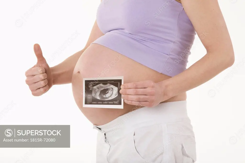 Pregnant woman holding sonogram image, showing thumbs up sign, mid section