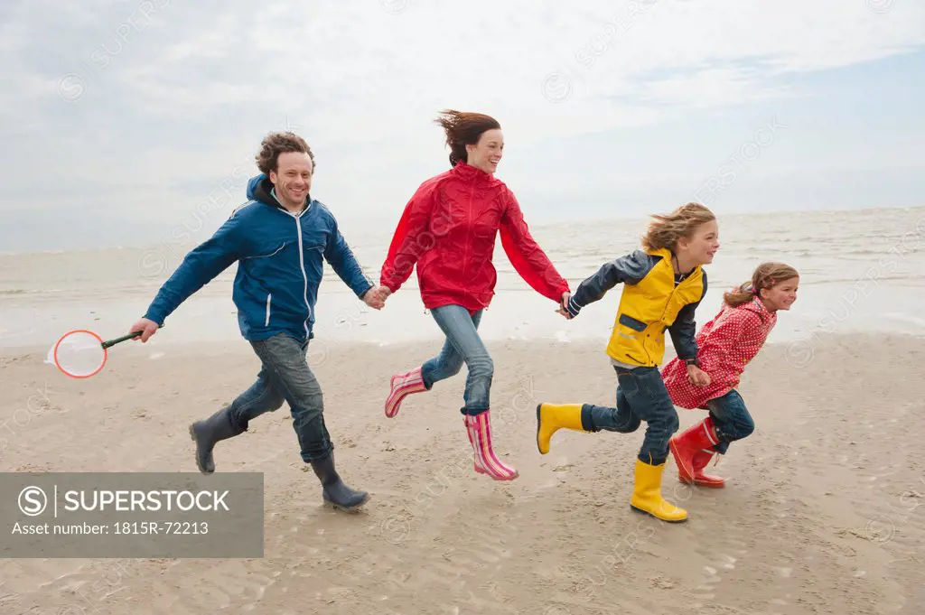 Germany, St. Peter_Ording, North Sea, Family holding hands and running on beach
