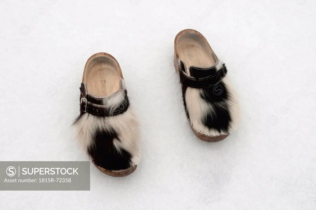 Pair of wooden shoes with cowskin in snow, winter.