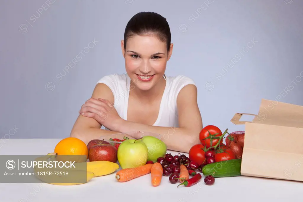 Young woman sitting with fruits and vegetables, smiling, portrait
