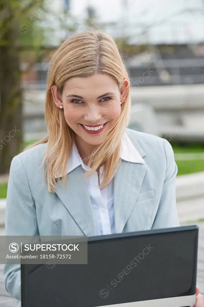Germany, Hamburg, Businesswoman smiling at harbour using laptop