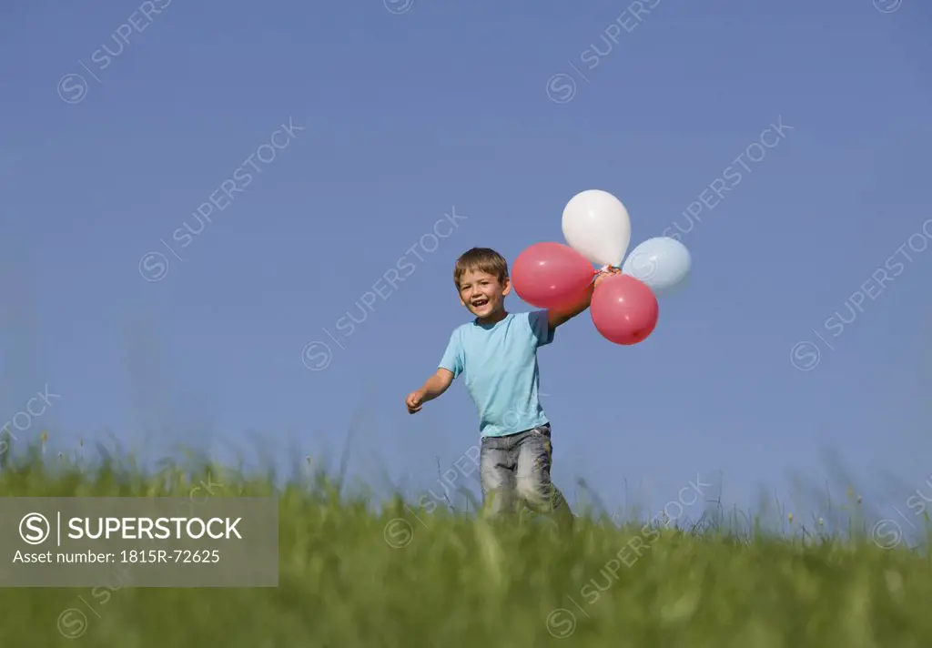 Austria, Mondsee, Boy 2_3 running through meadow holding balloons
