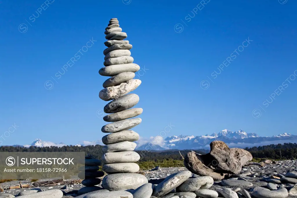 New Zealand, South Island, West Coast, Piles of Stones in beach with mountains in background