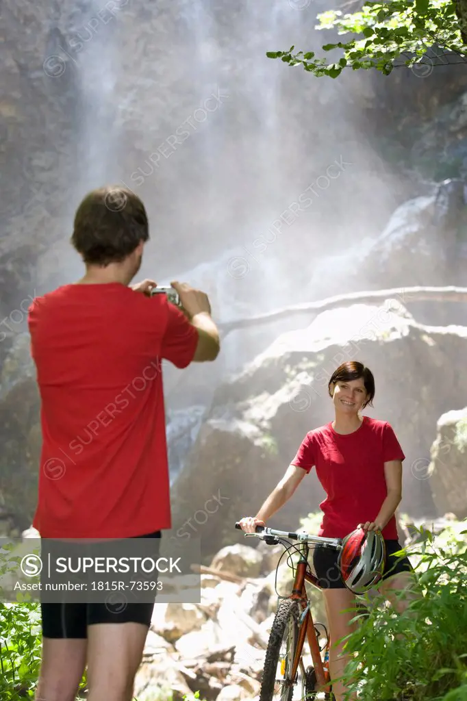 Austria, Salzkammergut, Mondsee, Young man taking photo of woman with waterfall in background