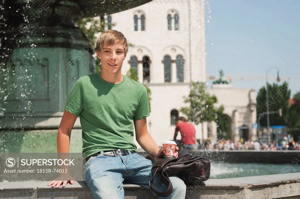 Germany, Munich, Karlsplatz, Young man sitting and looking away