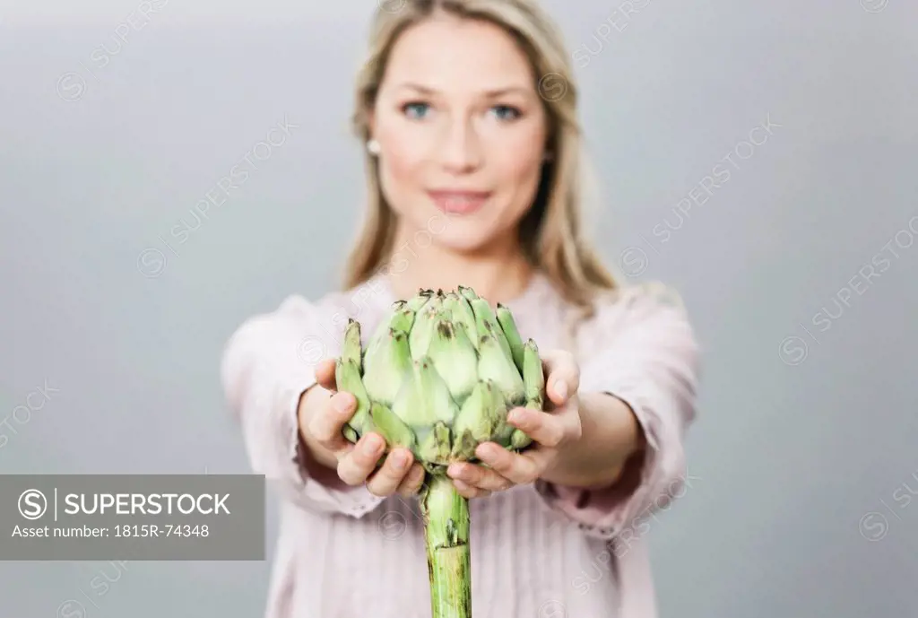 Mid adult woman holding artichoke, portrait