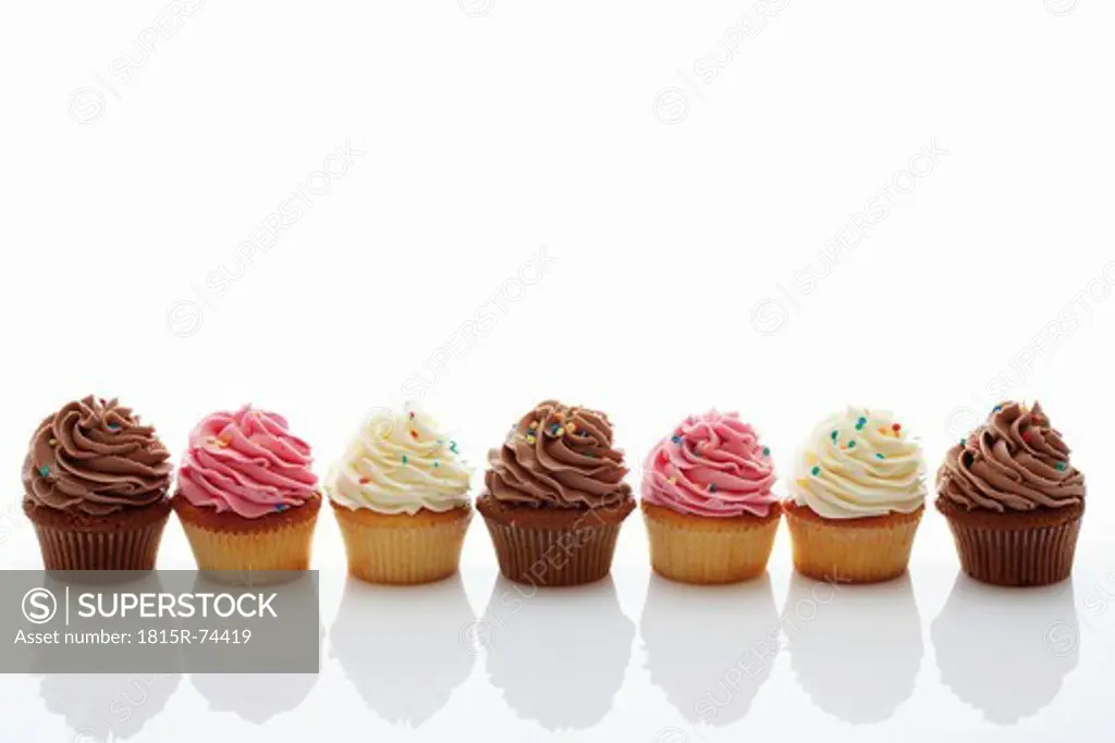 Close up of strawberry, vanilla and chocolate buttercream cupcakes against white background