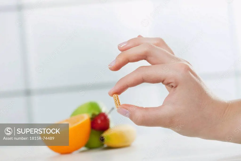 Germany, Cologne, Human hand holding diet pill with fruits in background
