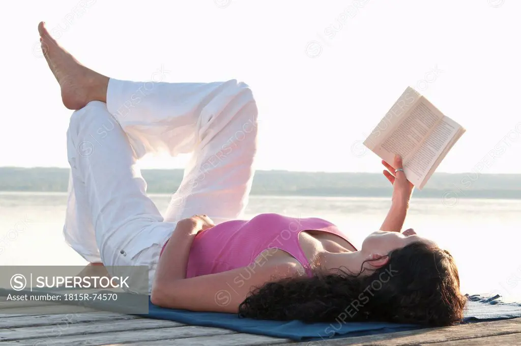 Mid adult woman lying on jetty and reading book