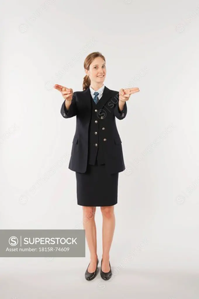 Young air stewardess with gun sign against white background, smiling, portrait