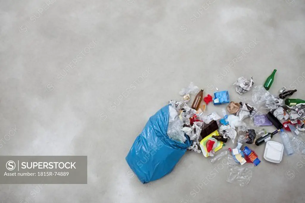 Garbage spilling from plastic bag on gray background