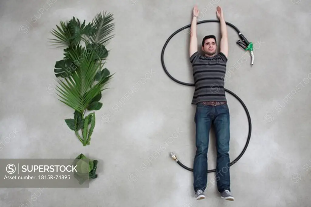 Young man lying on industrial hose beside plant