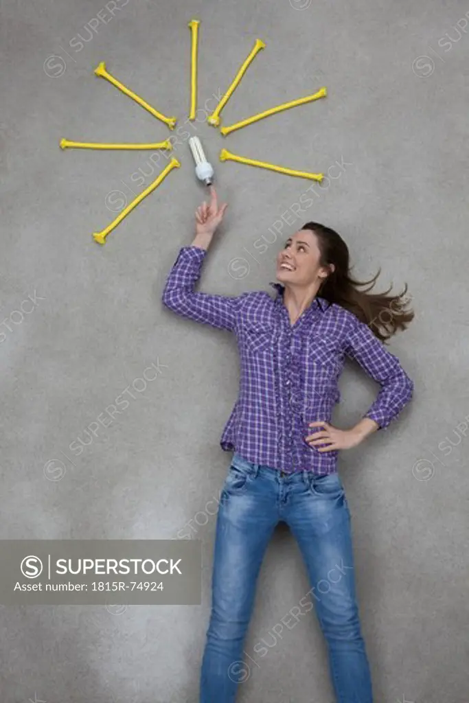 Mid adult woman pointing at electric bulb, smiling