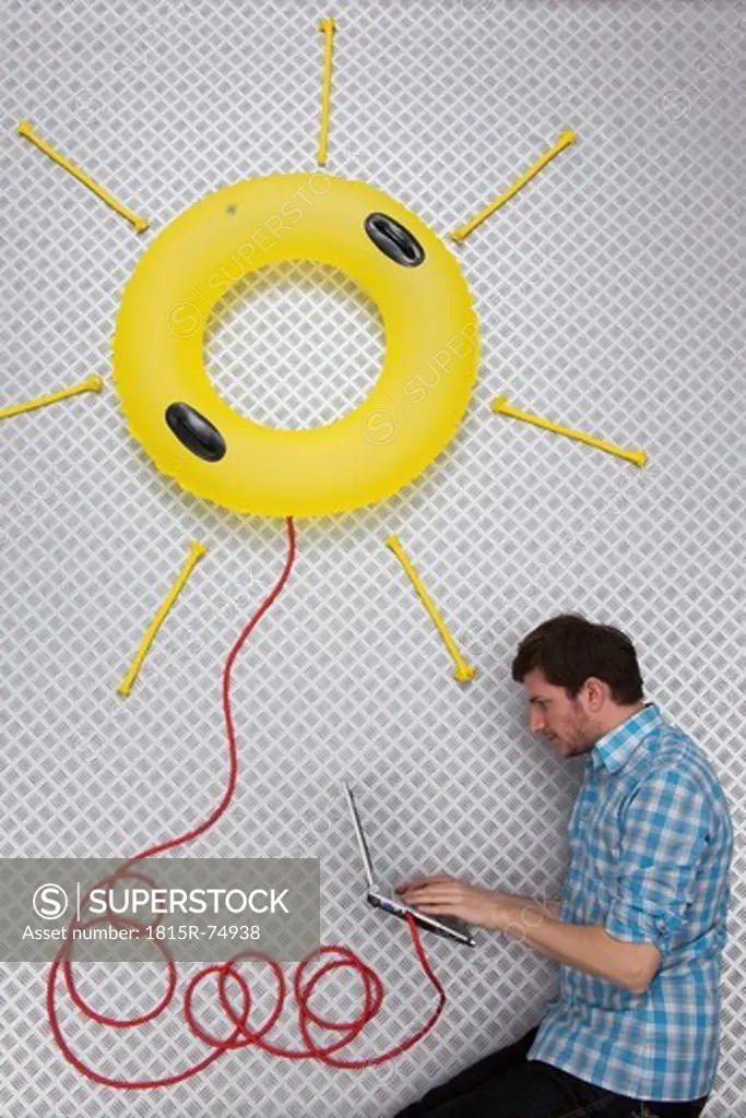Mid adult man using laptop connected to sun shape float