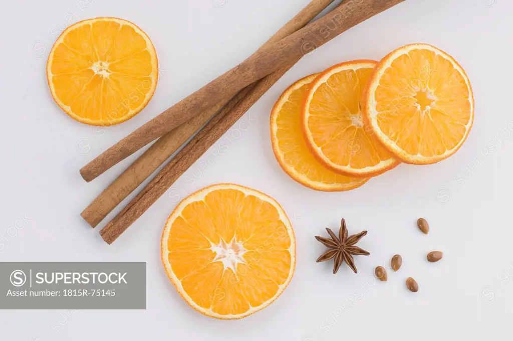 Close up of orange slice with star anise and cinnamon against white background
