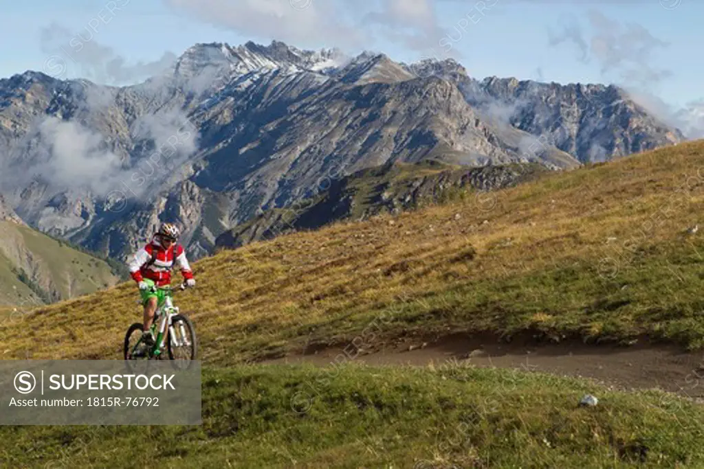 Italy, Livigno, View of woman riding mountain bike uphill
