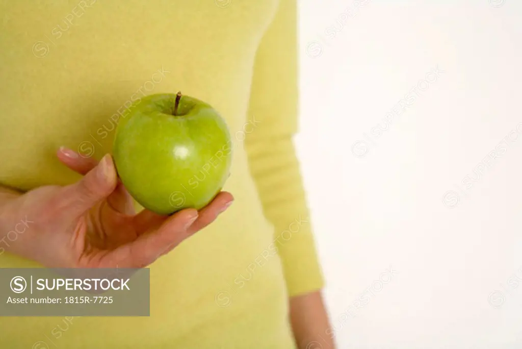 Young woman holding apple, mid section, close-up