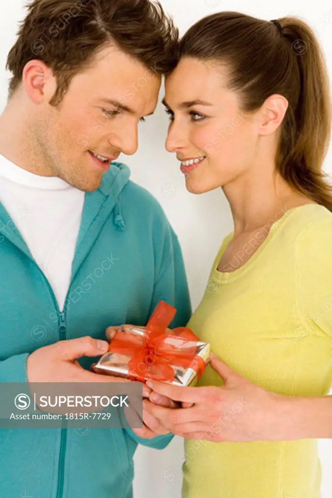 Young couple holding gift, close-up, smiling