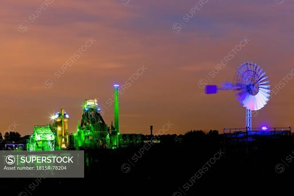 Germany, Nordrhein_Westfalen, Duisburg, Duisburg_Nord Landscape Park, View of illuminated blast furnace and wind mill of industrial plant at night