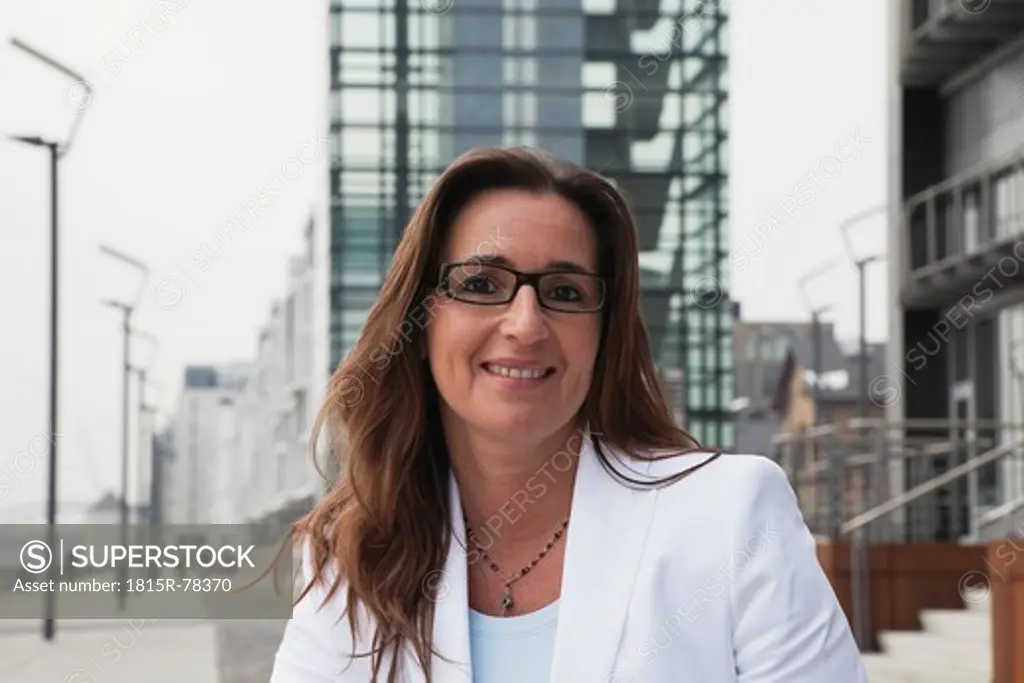 Germany, Cologne, Businesswoman with spectacles next to Rhine river and crane house in background, smiling, portrait