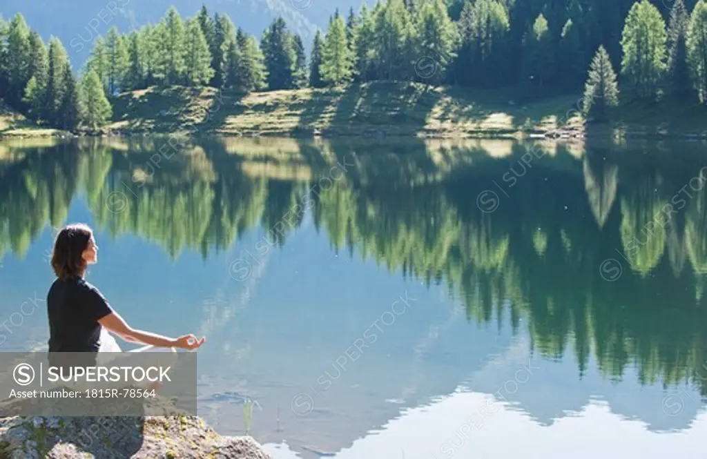 Austria, Styria, Mid adult woman meditating at lake duisitzkar in schladming