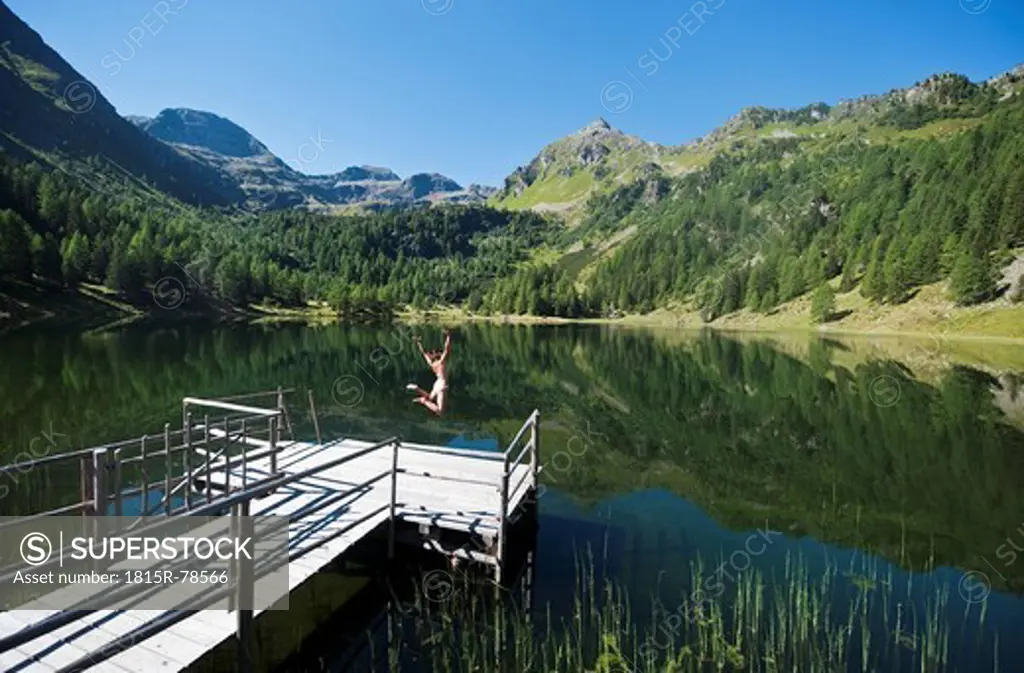 Austria, Styria, Mid adult woman jumping into lake duisitzkar in schladming