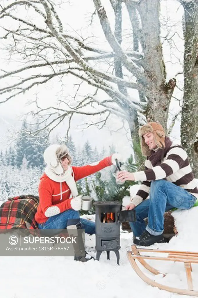 Austria, Salzburg Country, Flachau, Young man and woman making tea and sitting besides stove in winter