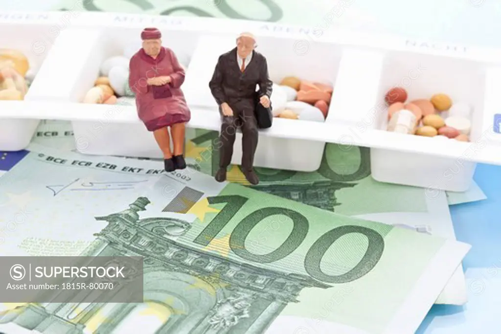 Figurines sitting on pill organizer with 100 euro notes