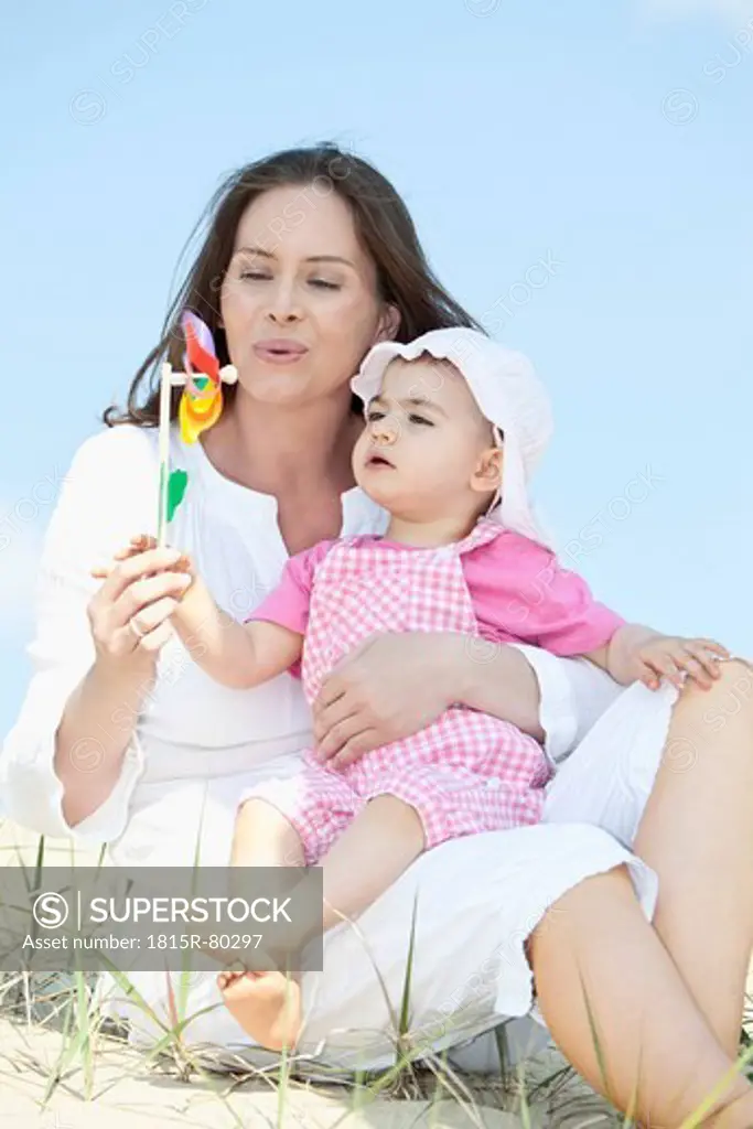 Germany, Bavaria, Mother blowing paper windmill with baby girl sitting on her lap