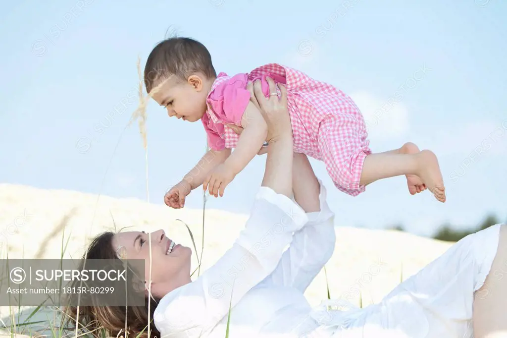 Germany, Bavaria, Mother lying and holding aloft baby girl