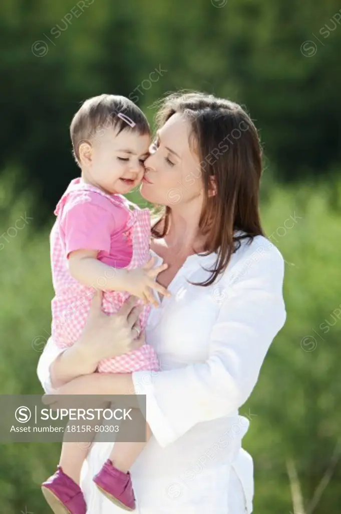 Germany, Bavaria, Mother kissing her baby girl, smiling