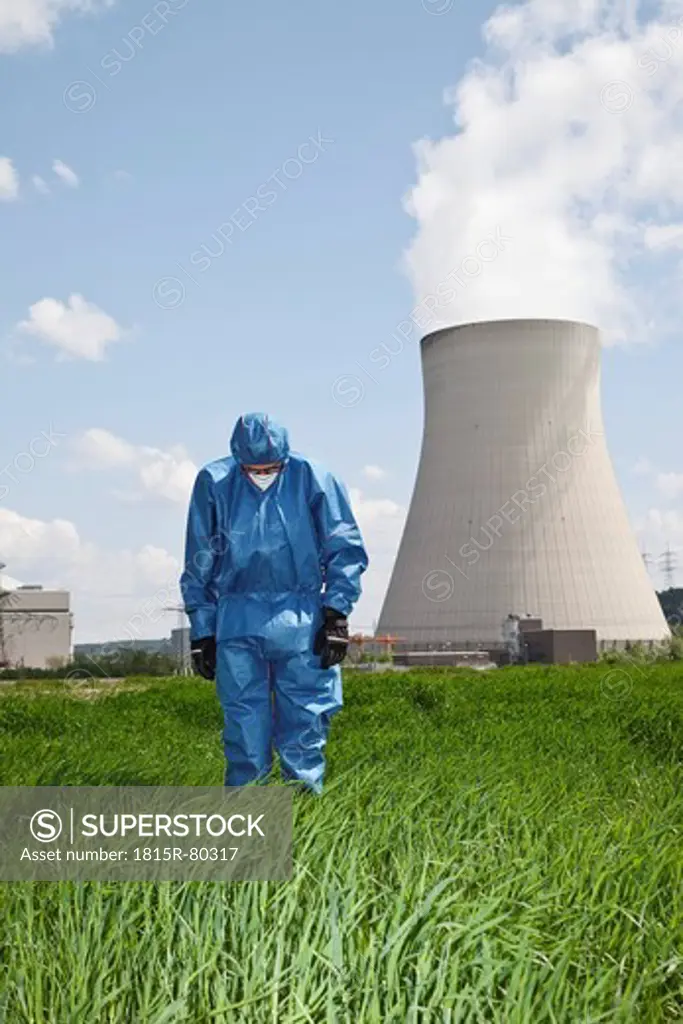 Germany, Bavaria, Unterahrain, Man with protective workwear standing and looking down in field at AKW Isar