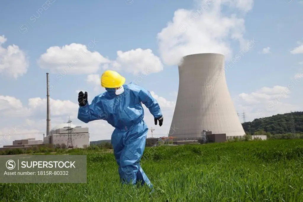 Germany, Bavaria, Unterahrain, Man with protective workwear running in field at AKW Isar