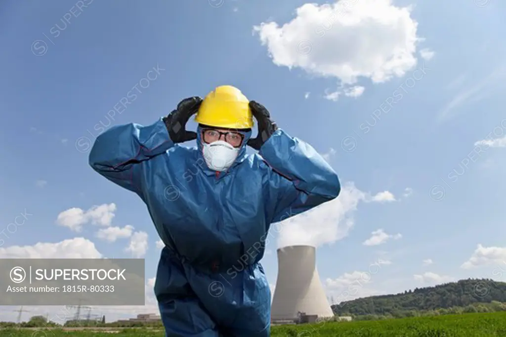 Germany, Bavaria, Unterahrain, Man with protective workwear covering his ears in field at AKW Isar