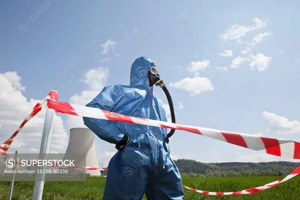 Germany, Bavaria, Unterahrain, Man with protective workwear standing in field at AKW Isar and cordon tape in foreground