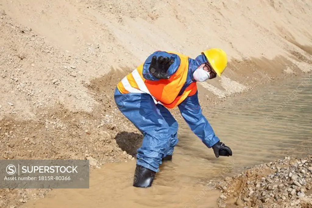 Germany, Bavaria, Man in protective workwear searching in water stream