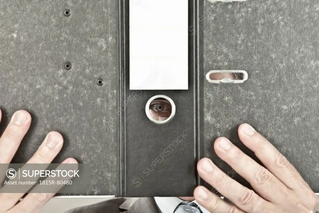 Close up of mature businessman looking through hole in ring binder