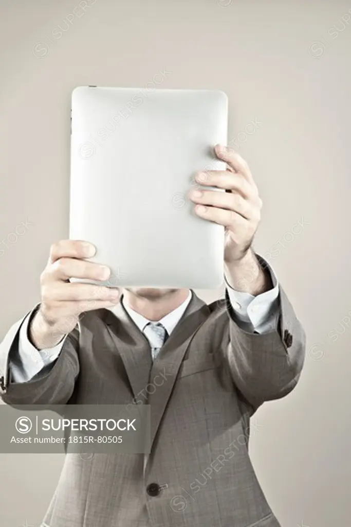 Close up of businessman holding ipad in front of his face against grey background