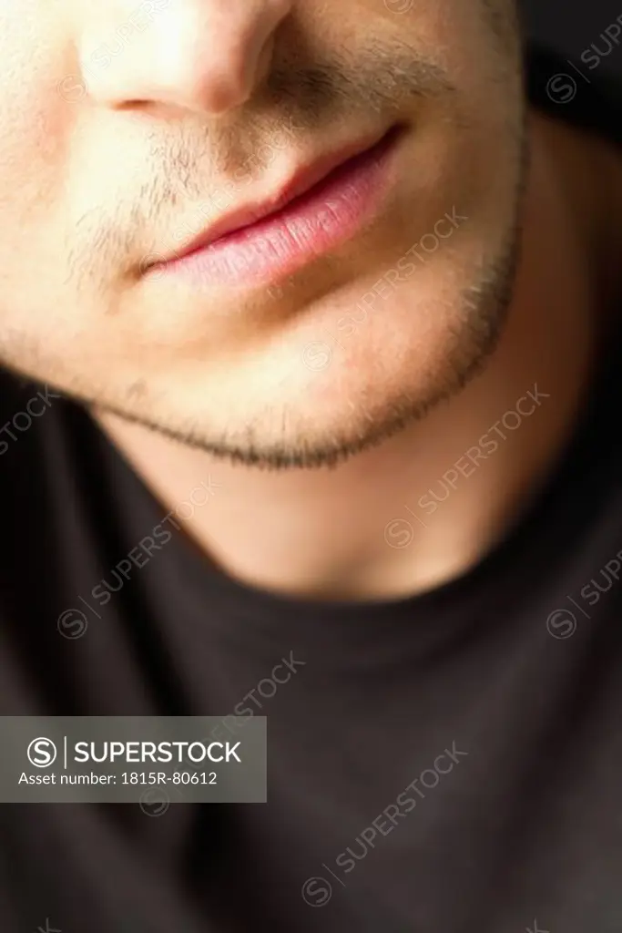 Lips of young man with stubble against black background, close up