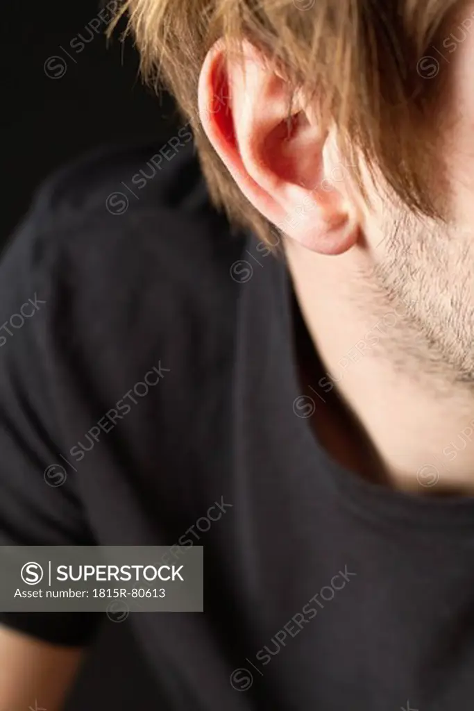 Ear of young man with stubble against black background, close up
