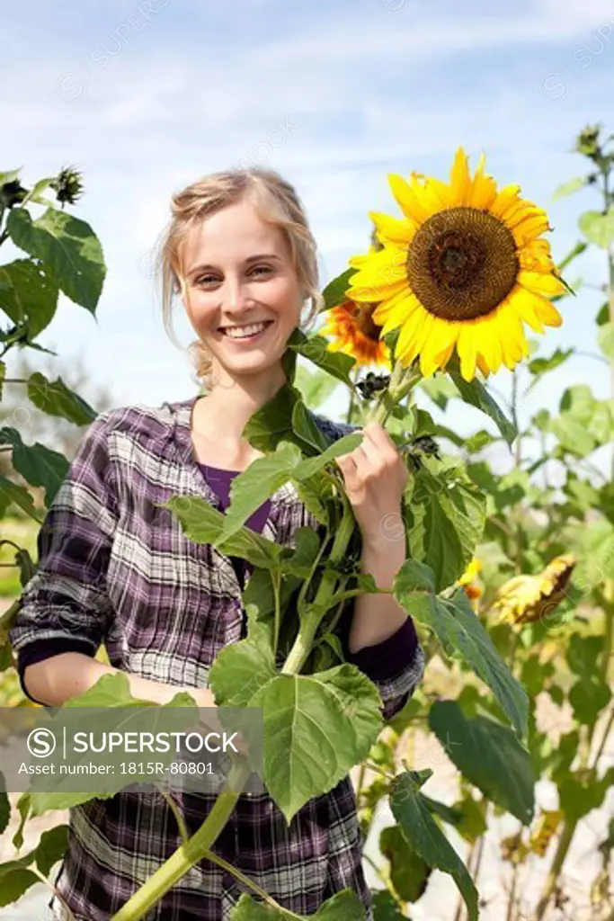 Germany, Saxony, Young woman with sunflower, smiling