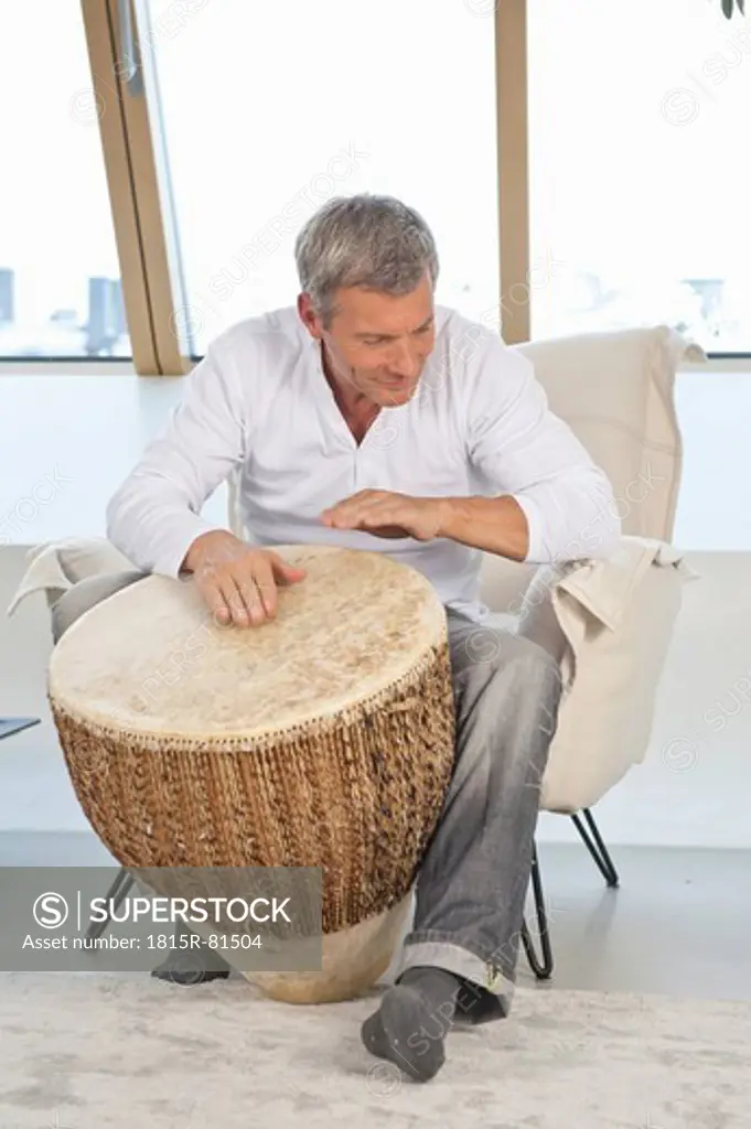 Germany, Munich, Mature man playing drum at home