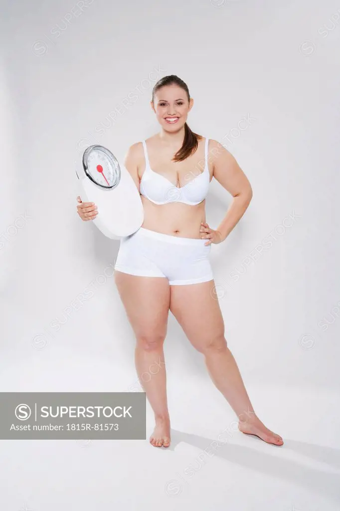 Young chubby woman with bathroom scales, smiling, portrait