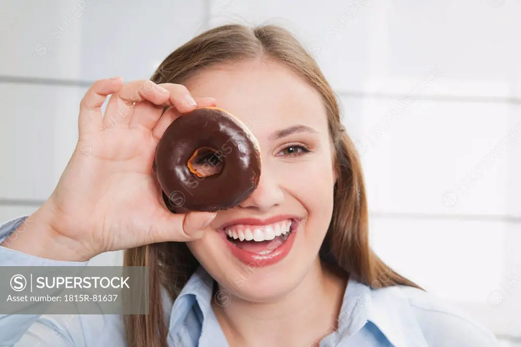 Germany, Cologne, Young woman watching through donut, smiling, portrait