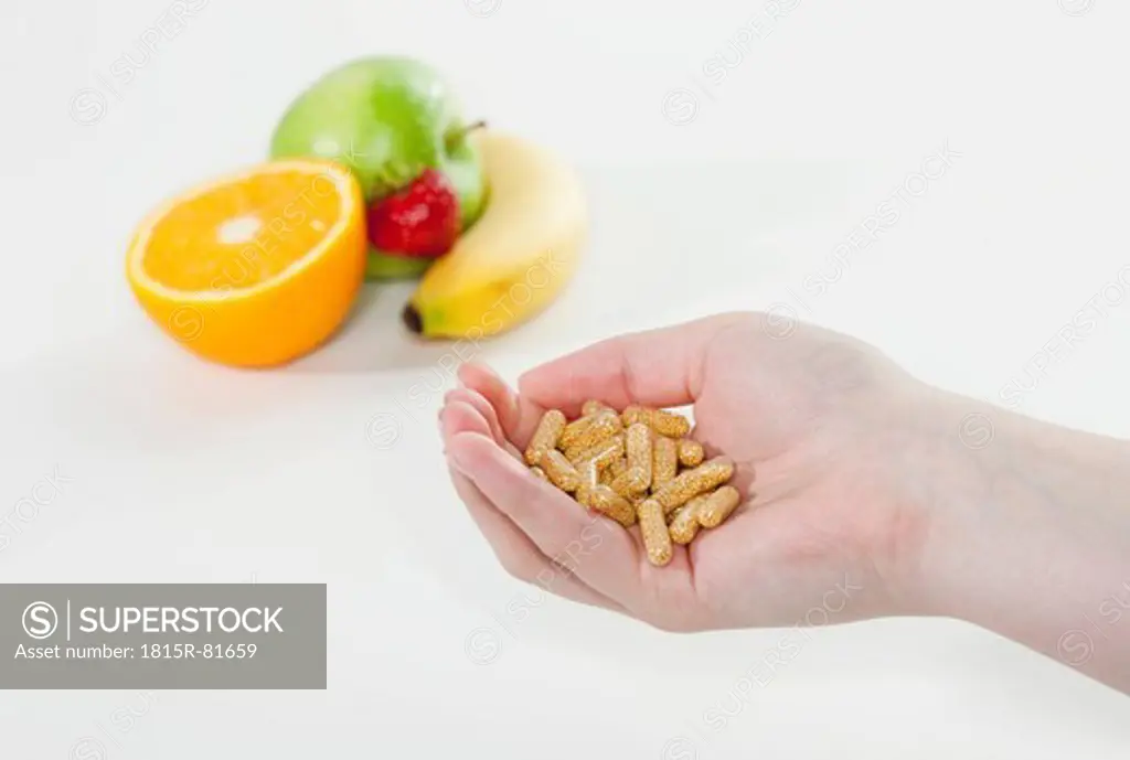 Germany, Cologne, Human hand holding pill with fruits in background