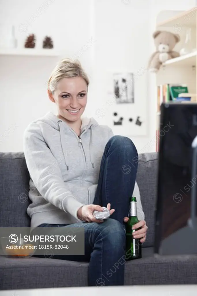 Germany, Munich, Young woman watching tv, smiling