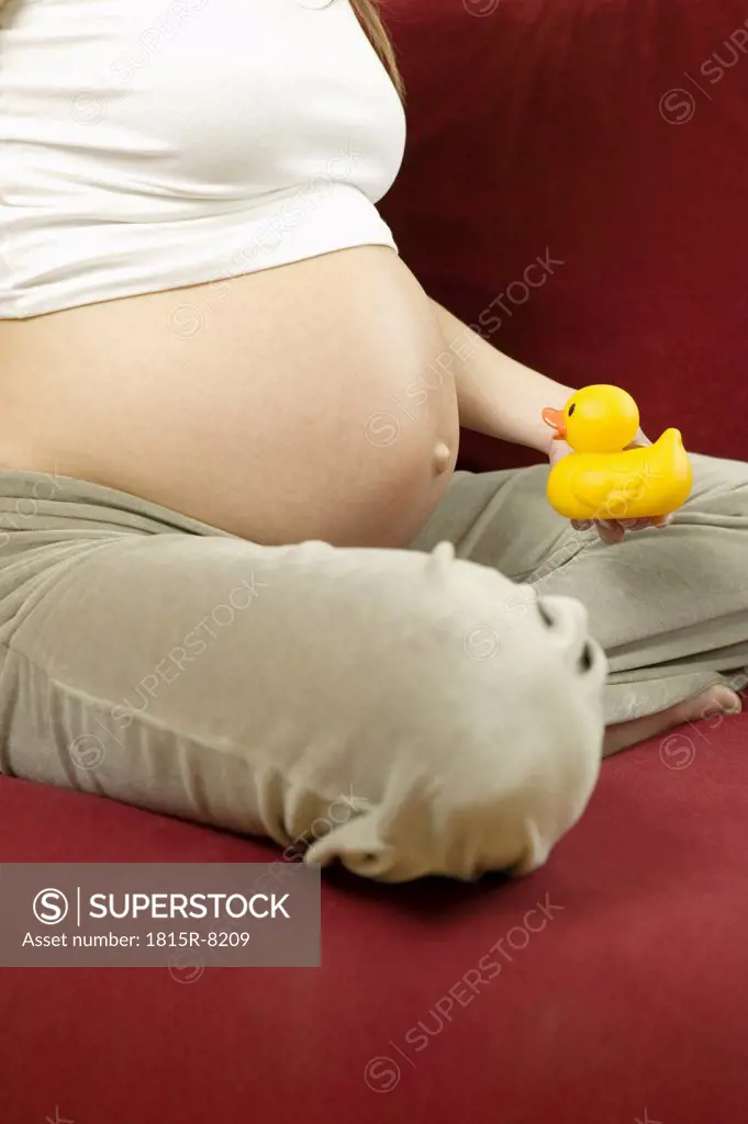 Pregnant woman holding rubber duck, low section